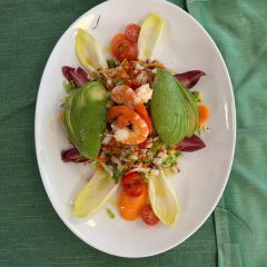 Ensalada tropical con aguacate, langostinos, endivias y vegetales frescos sobre mantel verde