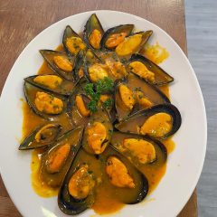 Mejillones en salsa marinera servidos en plato ovalado sobre mesa de madera